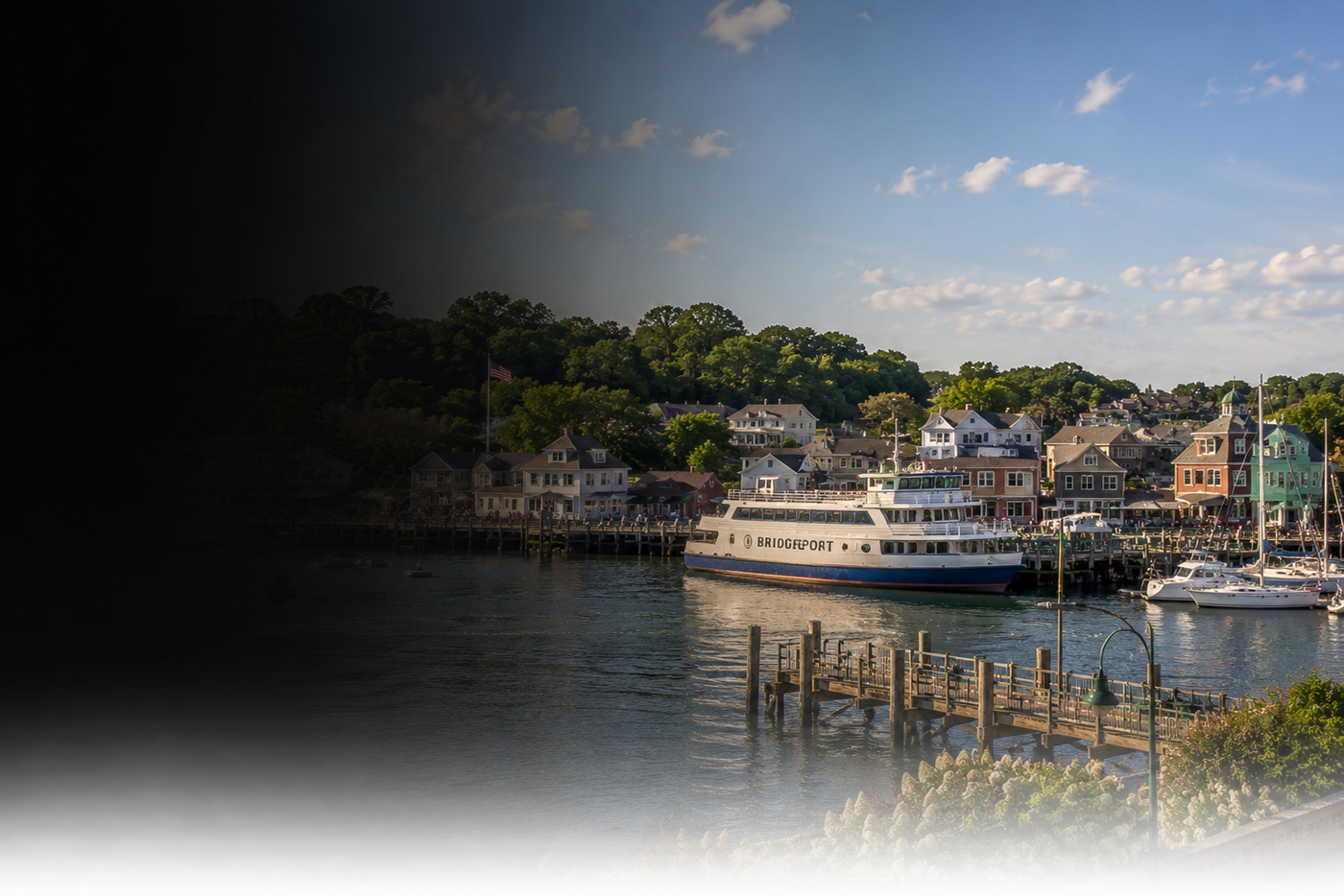 Harbor scene with a boat docked at a pier, surrounded by buildings and trees.