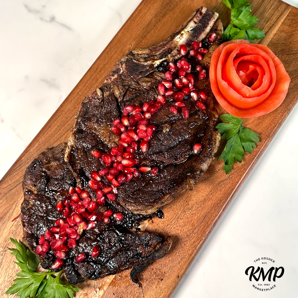 Grilled steak with pomegranate seeds on a wooden board, garnished with parsley and a carrot rose, on a marble surface.